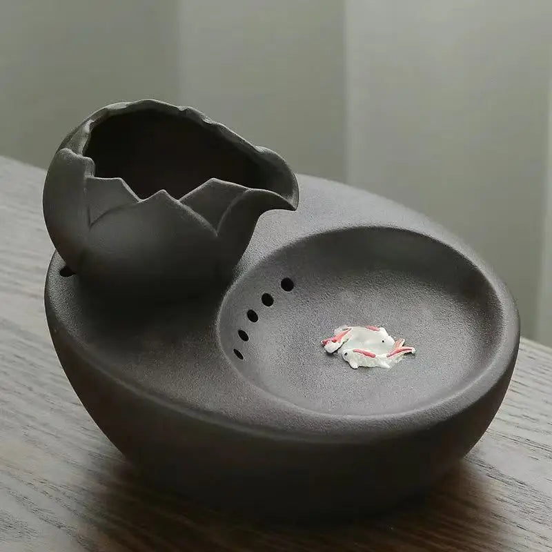 Cendrier en argile noir en forme d'œuf avec un petit pot fissuré, design moderne.